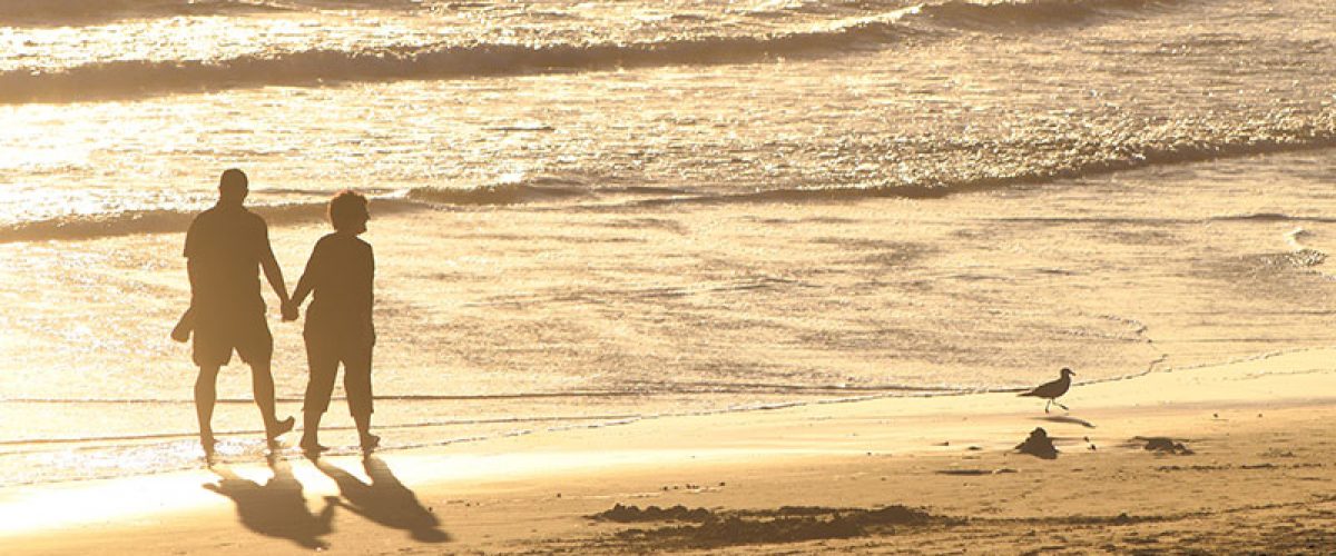 older-couple-holding-hands-and-walking-along-the-golden-beach-at-golden-hour-right-before-sunset_t20_4loEg_resize